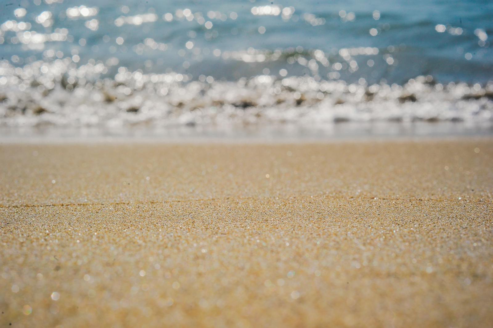 Close-up of sandy beach with ocean waves and sparkling water in the background.
